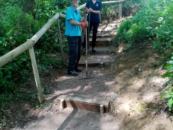 Two volunteers standing on steps with rakes