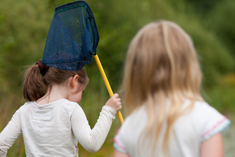 Two children walking away from the camera with a pond dipping net