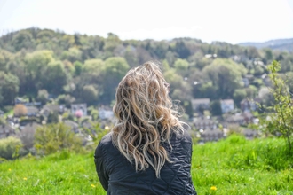 Picture of the back of a lady with flowing hair sitting down as she looks out over the countryside