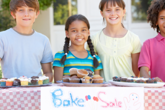 4 children standing by a table with treats they're selling for a bake sale