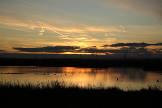 The sun setting over Oare Marshes, reflecting orange hues on the water.