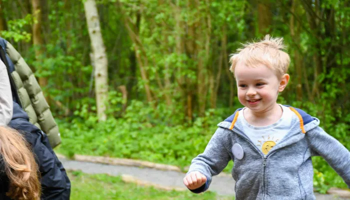 A child running towards the photographer, with grass and trees in the background