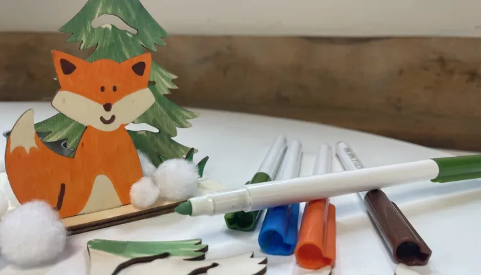 A partially made craft kit, with wooden fox and tree shapes and coloured pens.