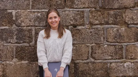 Katie Carr, Business Support Officer at KWT, standing with a laptop in front of a stone wall.