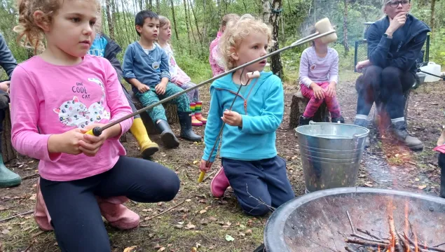 Children holding sticks with marshmallows on the fire at a forest school activity