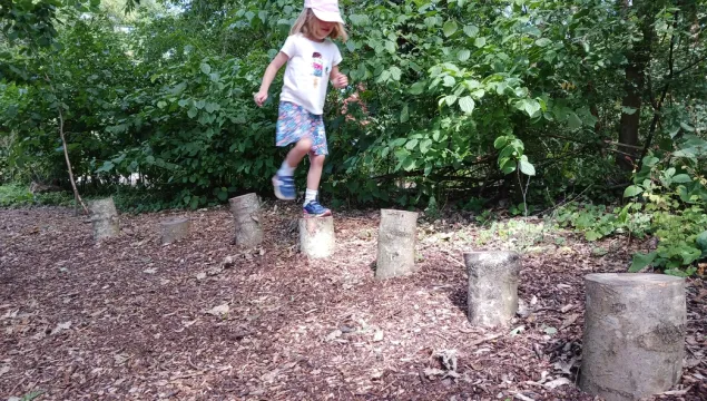 Child jumping on logs at forest school