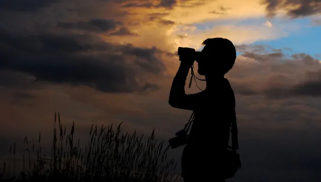 Silhouette of a person in the sunset looking out in the distance with binoculars