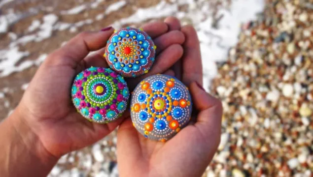 Someone holding three colourfully painted rocks in their hands.