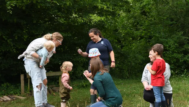 A group of toddlers and adults listening to a Kent Wildlife Trust tutor showing what has been found during a mini-beasting session.