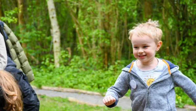 A child running towards the photographer, with grass and trees in the background