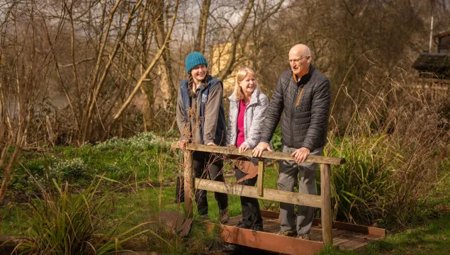 three people smiling and looking over a bridge 