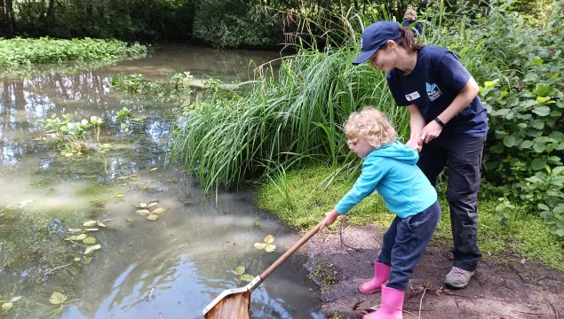 A child pond dipping, being supported by a member of KWT staff. 