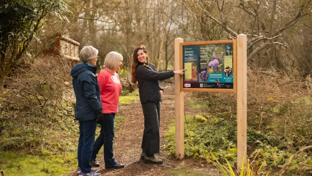 Three people standing and looking at a sign in a nature reserve.