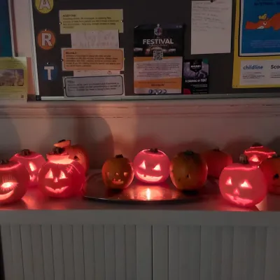 A row of carved pumpkins sat on top of a cabinet, with candles in them.