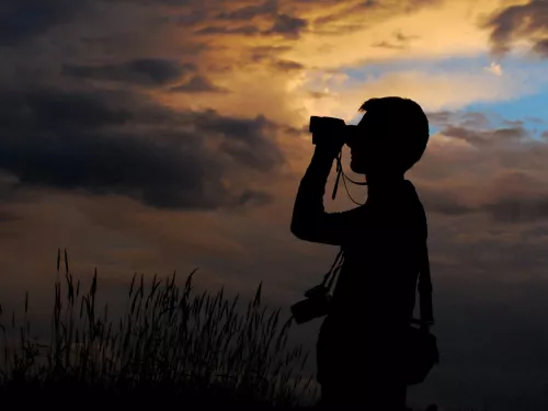 Silhouette of a person in the sunset looking out in the distance with binoculars
