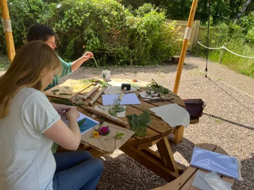 Two people sat outside using leaves and petals to make prints