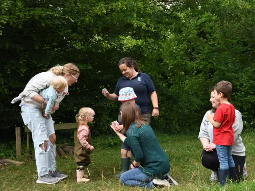 A group of toddlers and adults listening to a Kent Wildlife Trust tutor showing what has been found during a mini-beasting session.