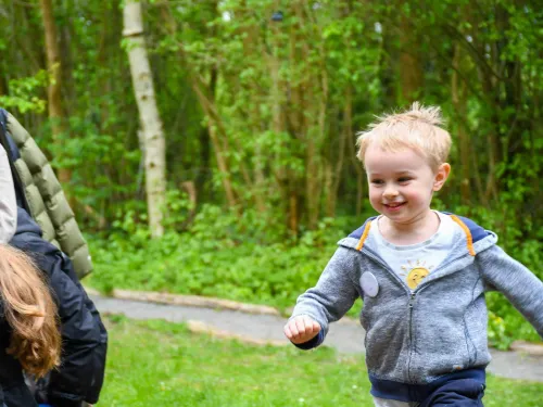 A child running towards the photographer, with grass and trees in the background