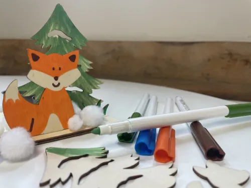A partially made craft kit, with wooden fox and tree shapes and coloured pens.