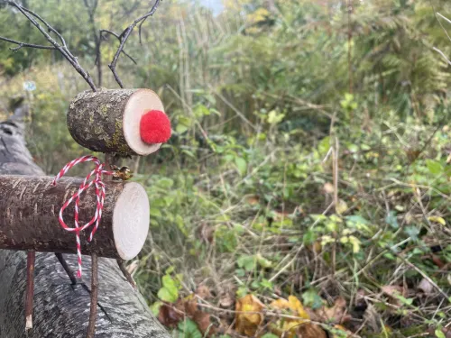 Two pieces of branch joined with twigs to make the shape of a reindeer, with a red pompom nose and ribbon around its neck.