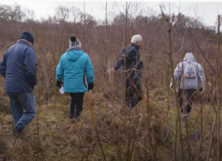 4 people in outdoor clothing walking across a nature reserve.