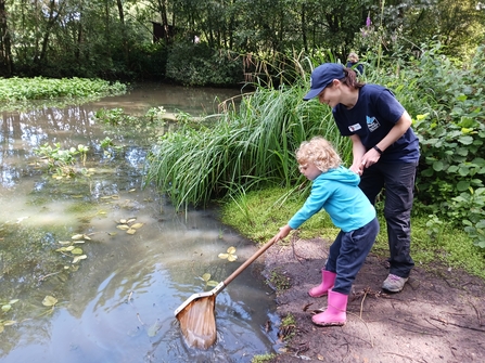 Tutor helps child to dip net into pond at Kent Wildlife Trust education centre